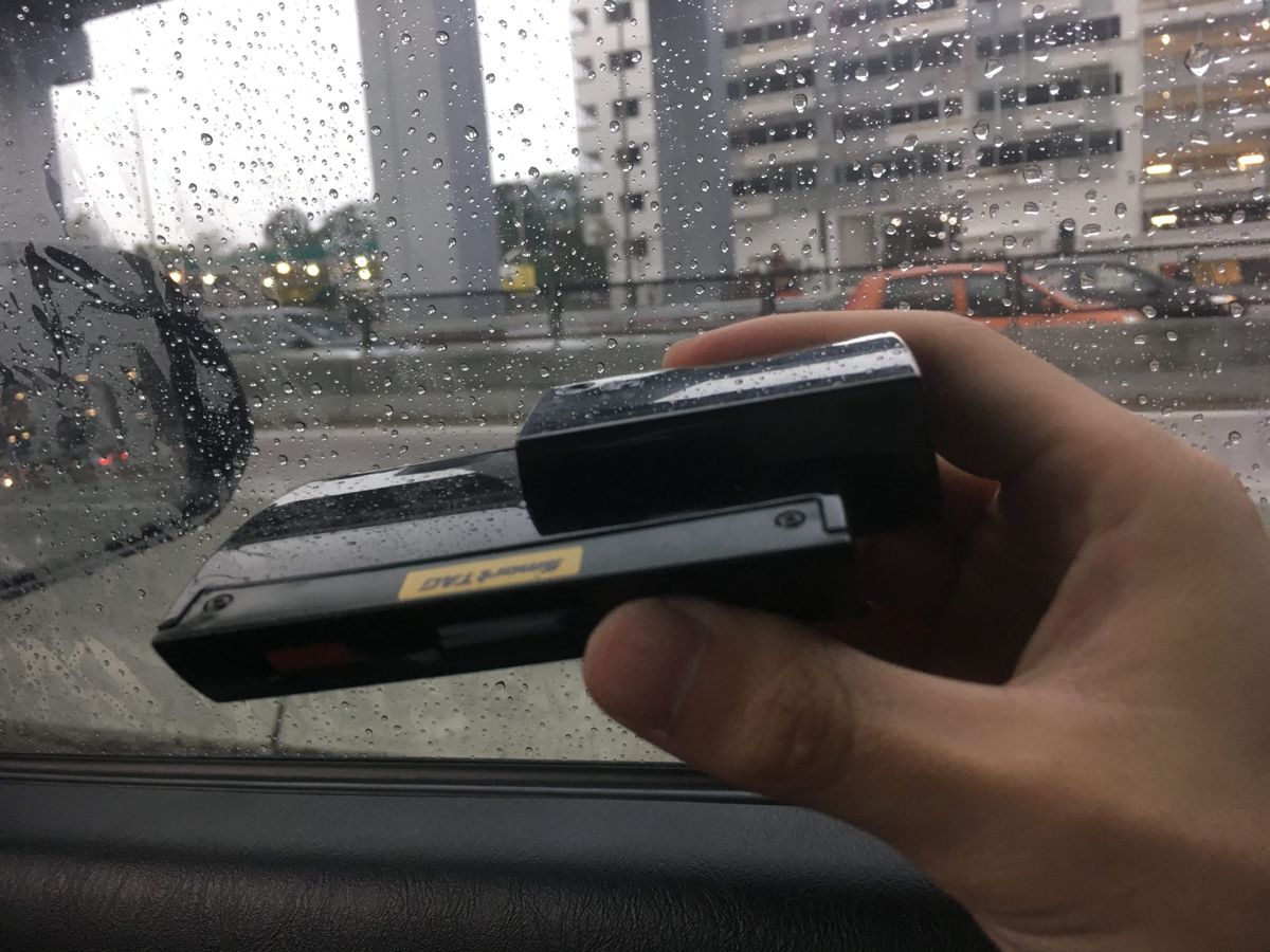 車内でSmartTAG車載機器を手に持ち、カード差込口側を自分に向けて窓ガラスにかざしているところ(筆者撮影)